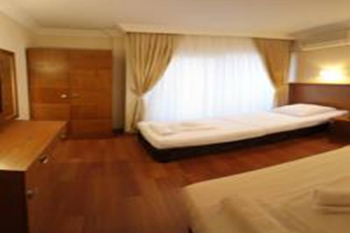 Habitación de hotel con una cama individual, cómoda de madera, mesita de noche y ventana con cortinas.