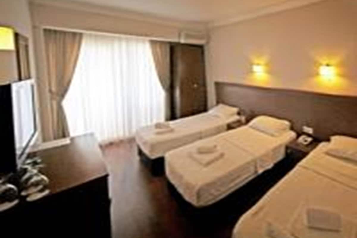 Habitación de hotel con dos camas individuales, un escritorio, una silla y una ventana con cortinas.