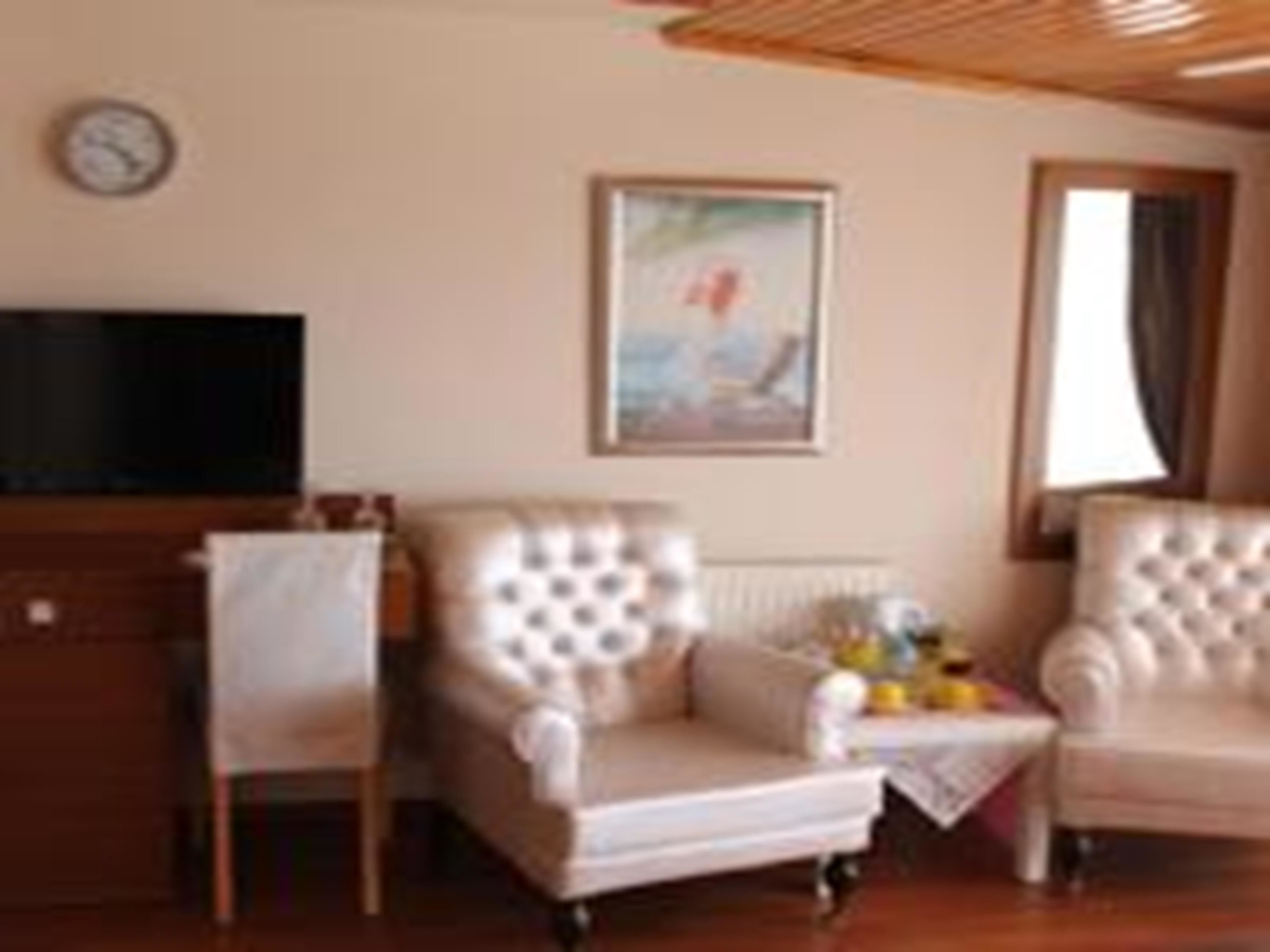 Un salón con dos sillones tapizados, una mesita con un jarrón, un reloj en la pared y un cuadro enmarcado.