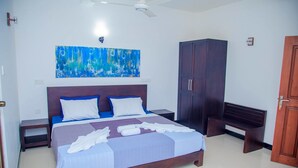 Una habitación de hotel con una cama grande, un armario, un banco y un ventilador de techo.