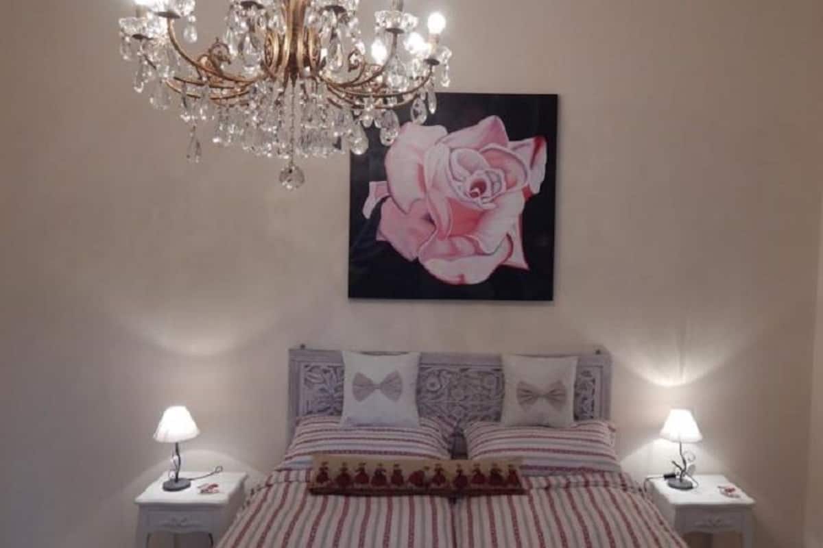 A bedroom with a chandelier, a large rose painting, striped bedding, and two bedside lamps.