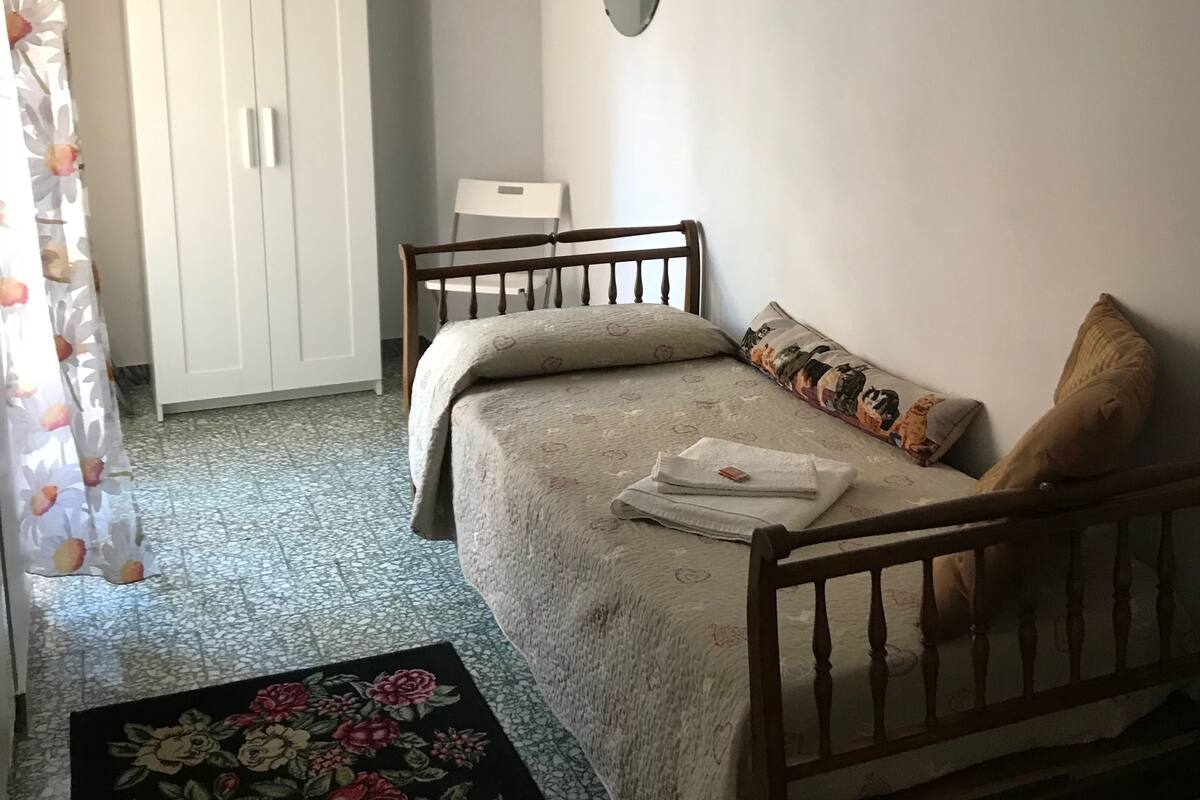 A bedroom with a bed, a wardrobe, a mirror, and a floral rug.