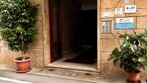A building entrance with a wooden door, a potted plant on the left, and several signs on the wall. - Musei Vaticani Rooms (Rome)
