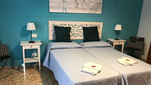 A double bed with a white bedspread, two bedside tables with lamps, a decorative headboard, and a painting of beachgoers on the wall. - Musei Vaticani Rooms (Rome)