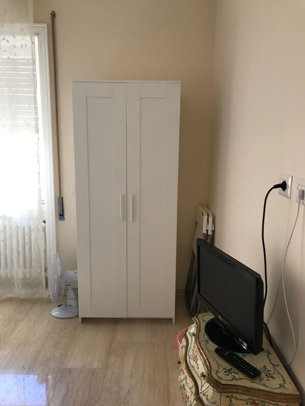 Una habitación con un armario blanco, un televisor sobre una mesita y un enchufe en la pared.