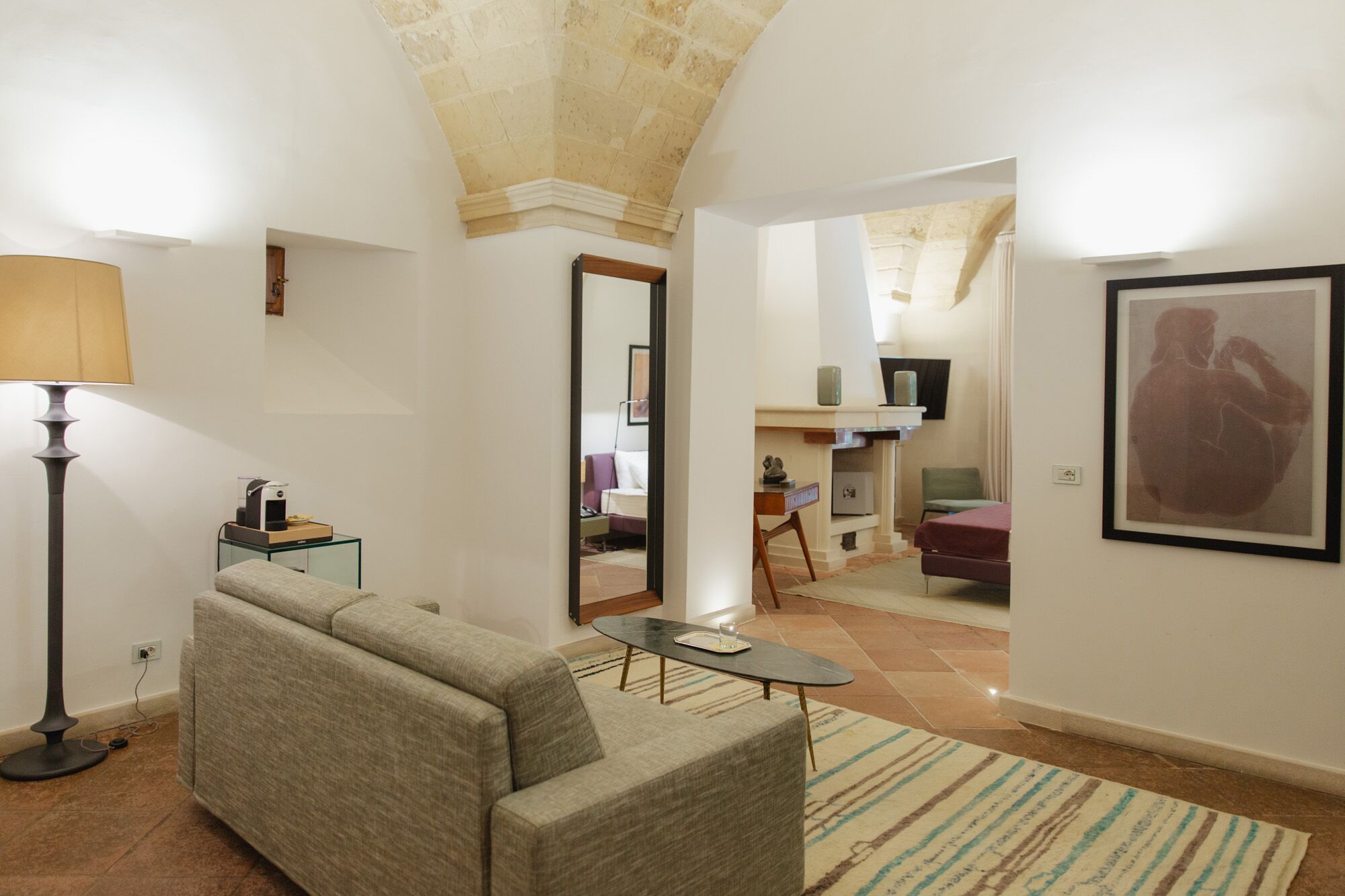 Un salon avec un canapé, une table basse, une lampe et un tapis. Il y a une télévision et un tableau accroché au mur.