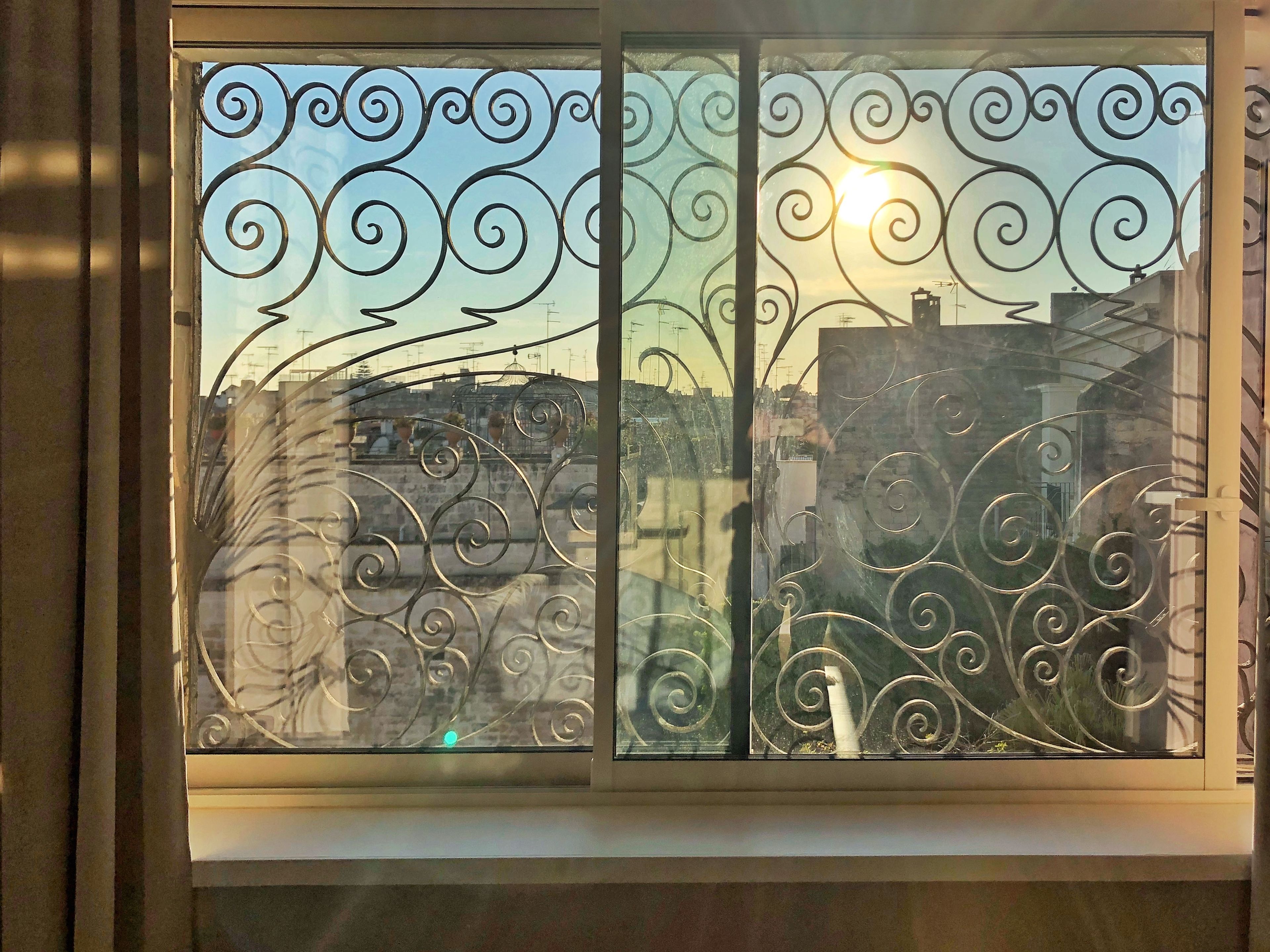 Una ventana con elaborada ornamentación metálica y vista a edificios al fondo.