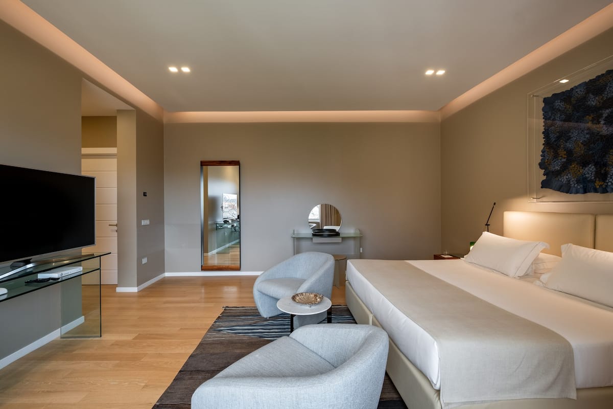 Een moderne hotelkamer met een groot bed, een flatscreen televisie, een zithoek met een kleine tafel, en een groot raam.