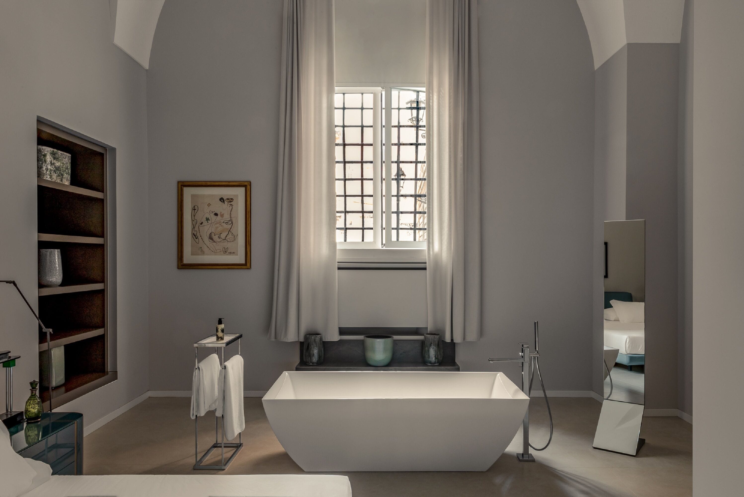 Ein modernes Badezimmer mit einer freistehenden Badewanne, einem Waschtisch mit Spiegel und einem Fenster mit Vorhängen.