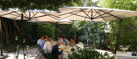 Un área de comedor al aire libre con mesas y sillas bajo sombrillas grandes, rodeada de exuberante vegetación.