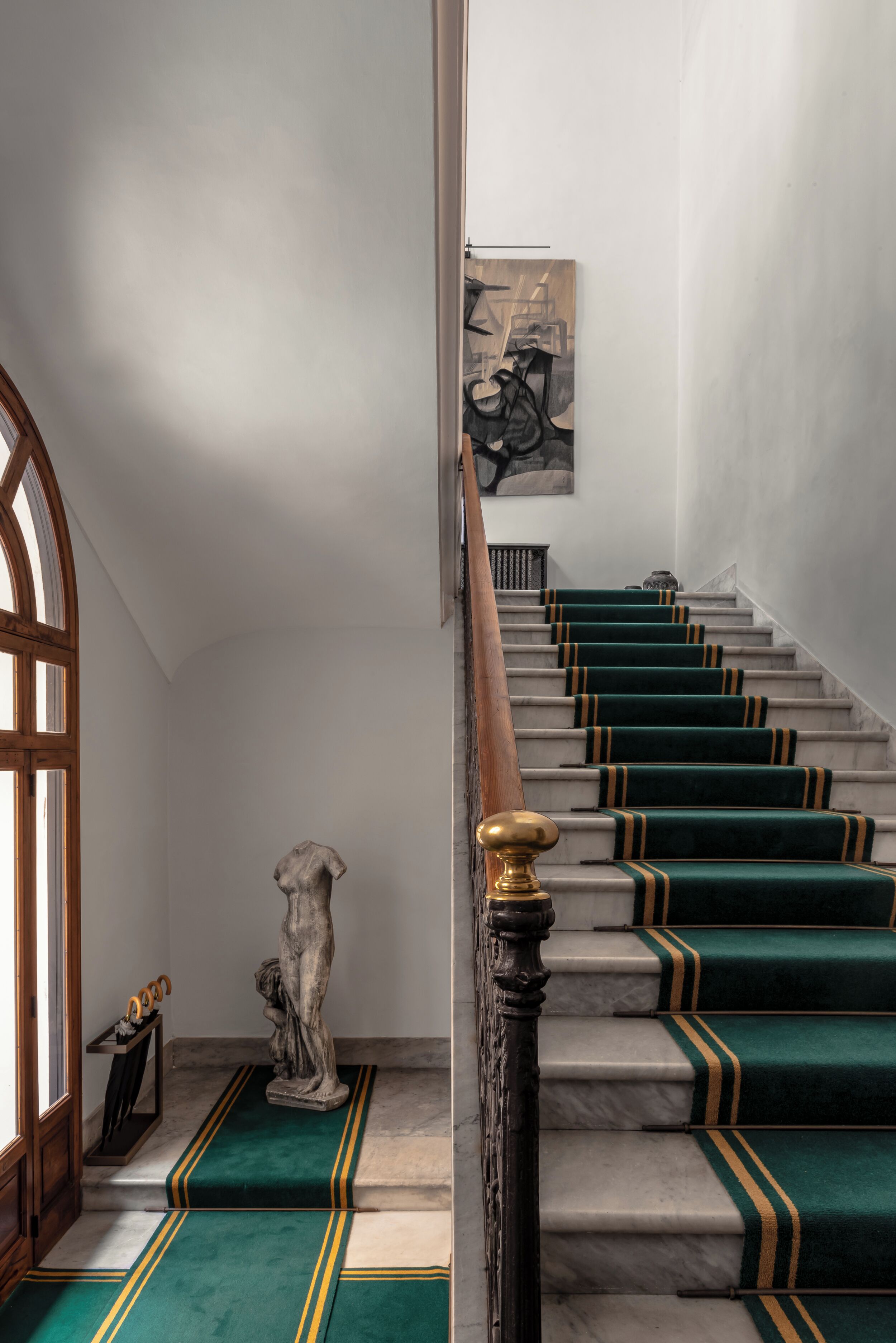 Una scala con gradini rivestiti di tappeto verde e strisce dorate, una ringhiera in marmo e una statua in fondo.