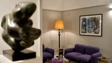 Un salon moderne avec des canapés violets, une table basse en verre, une lampe et une sculpture.