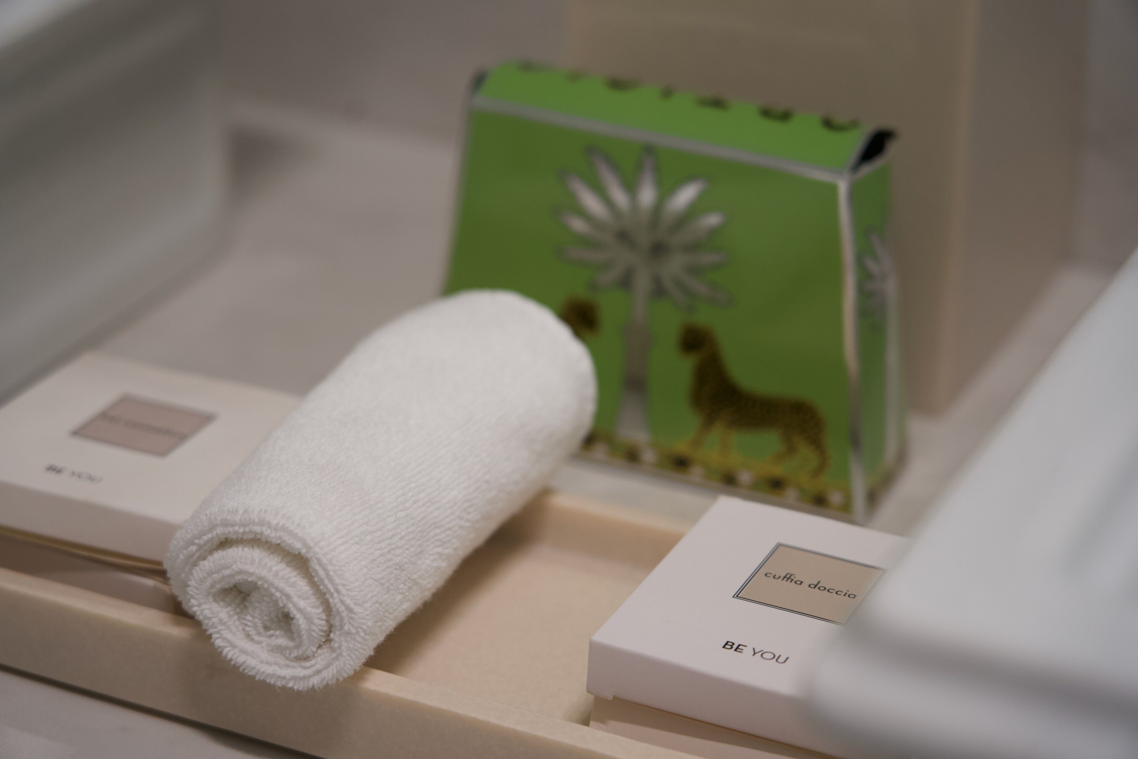 Une serviette blanche soigneusement enroulée et une boîte verte ornée d’une illustration de chameau, le tout posé sur un plateau beige.