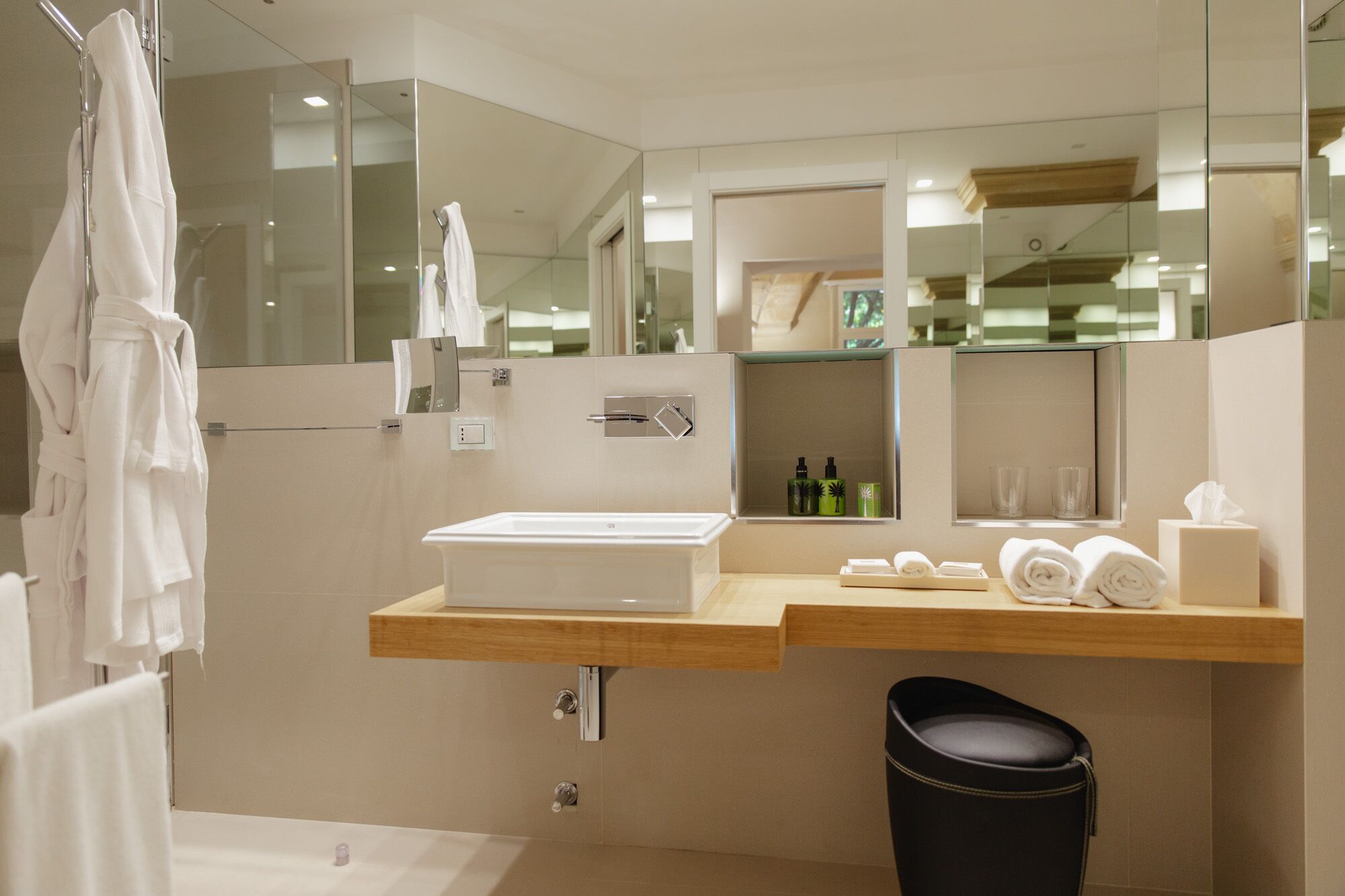 Une salle de bain moderne avec un grand miroir, un lavabo blanc et une poubelle noire.