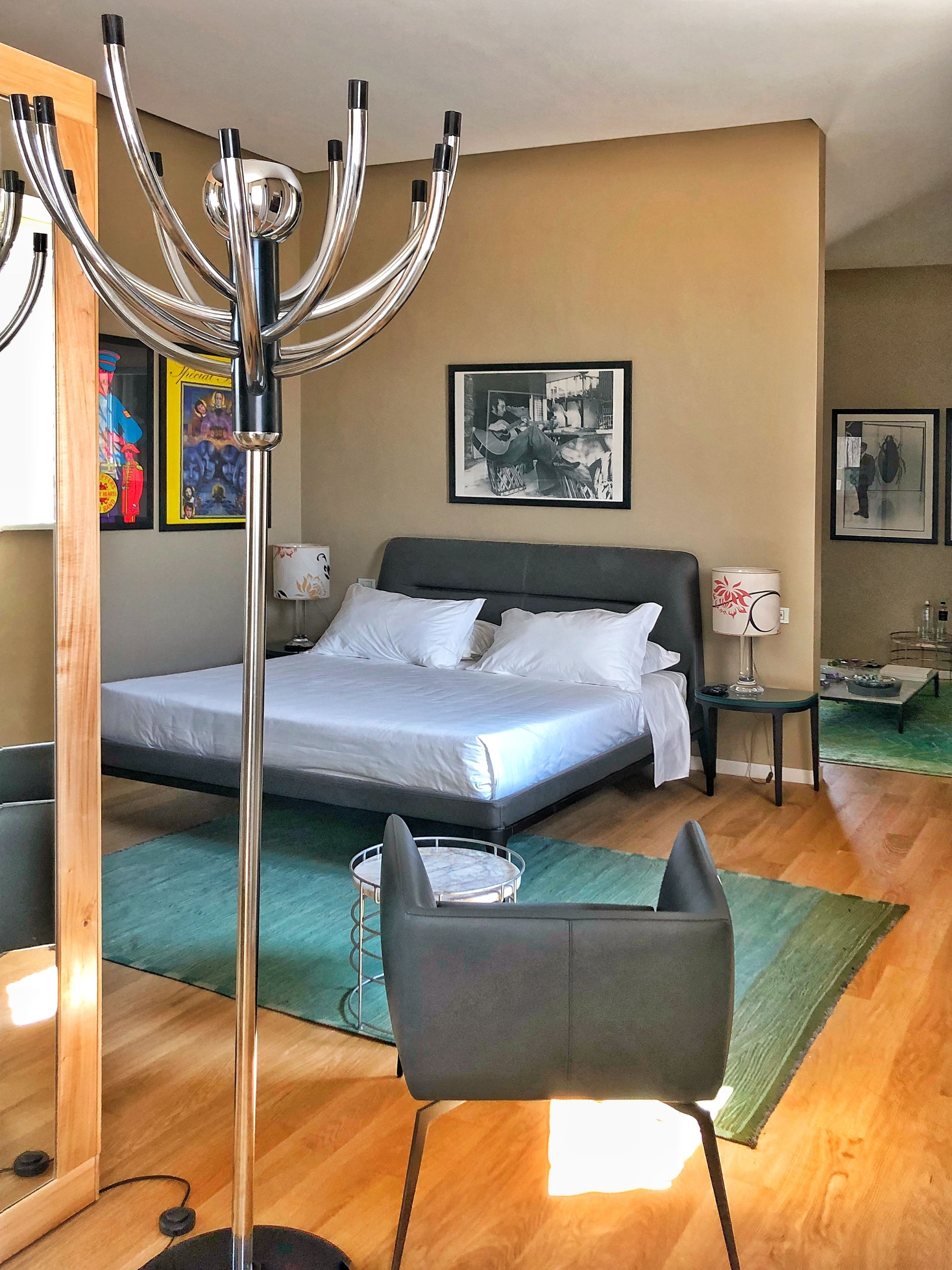 Una moderna camera d'albergo con un letto grande, una lampada da terra, una poltrona e opere d'arte alle pareti.