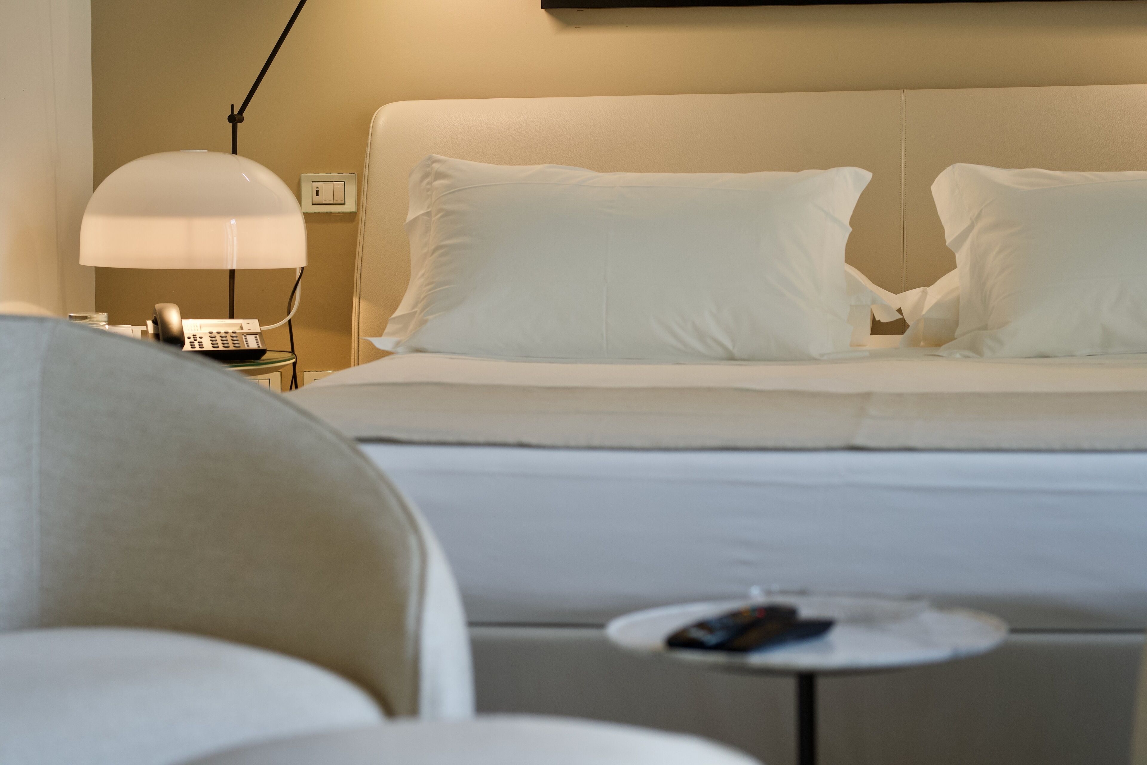 A hotel room with a bed, a nightstand with a lamp, and a small table with a remote control.