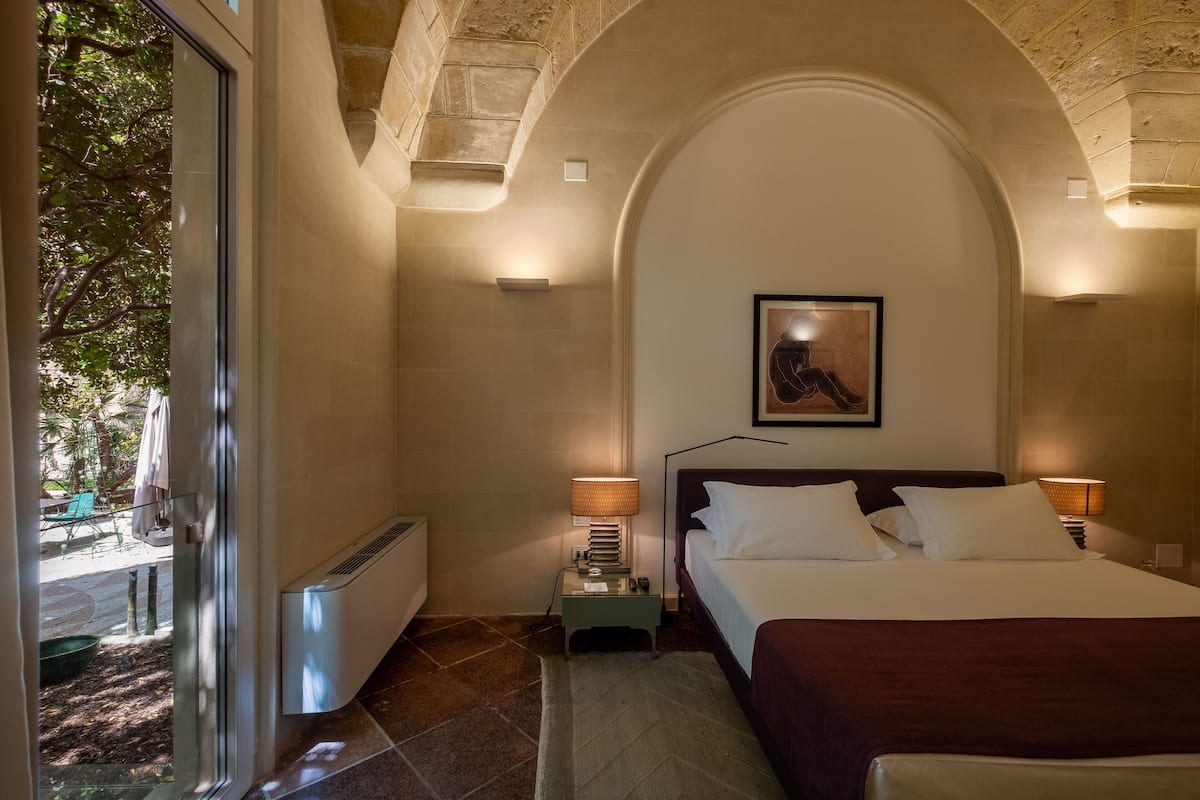 Een hotelkamer met een bed, nachtlampjes, een radiator en uitzicht op de omgeving.