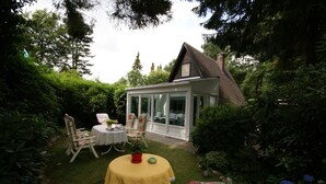 A cozy outdoor patio with a table and chairs, surrounded by lush greenery and a small house with a sloped roof. - **** Only roof house **** lovingly furnished    (Wiefelstede)