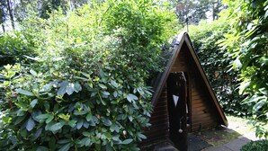 A small wooden structure with a sloped roof, surrounded by dense green foliage. - **** Only roof house **** lovingly furnished    (Wiefelstede)