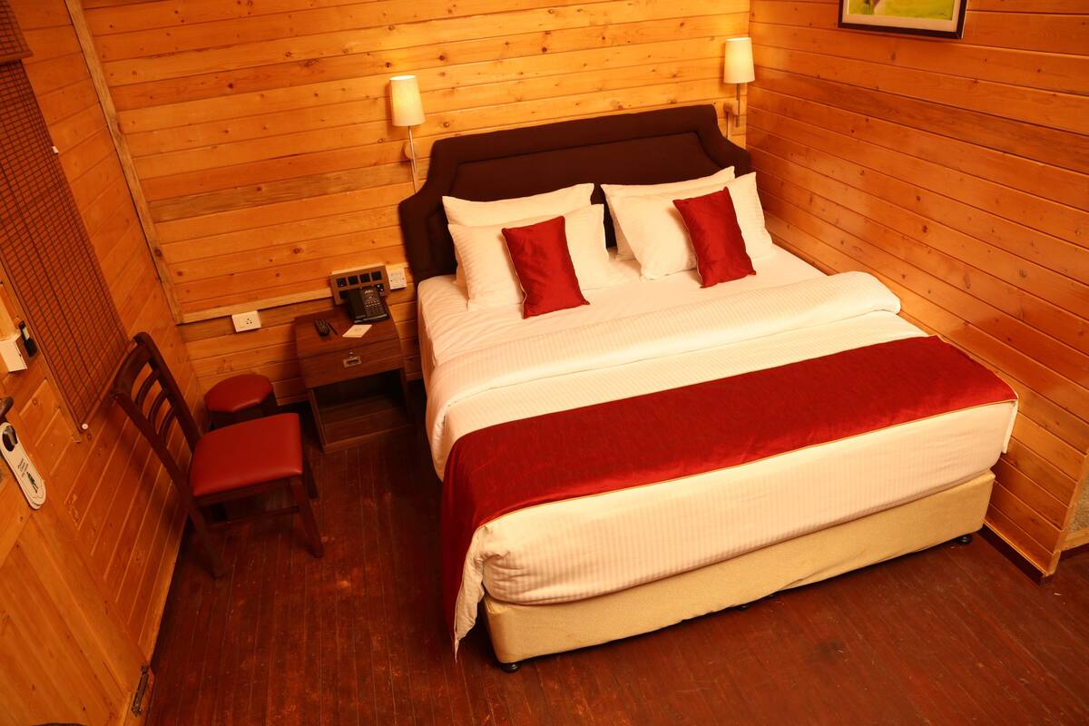 A wooden-paneled room with a bed, a nightstand, a chair, and a small table.