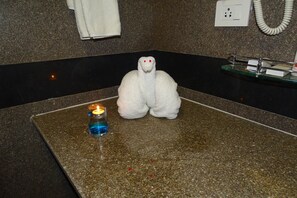 A bathroom with a towel sculpture, a lit candle, and a glass shelf with toiletries. - Kanva Star Resorts (Bengaluru)