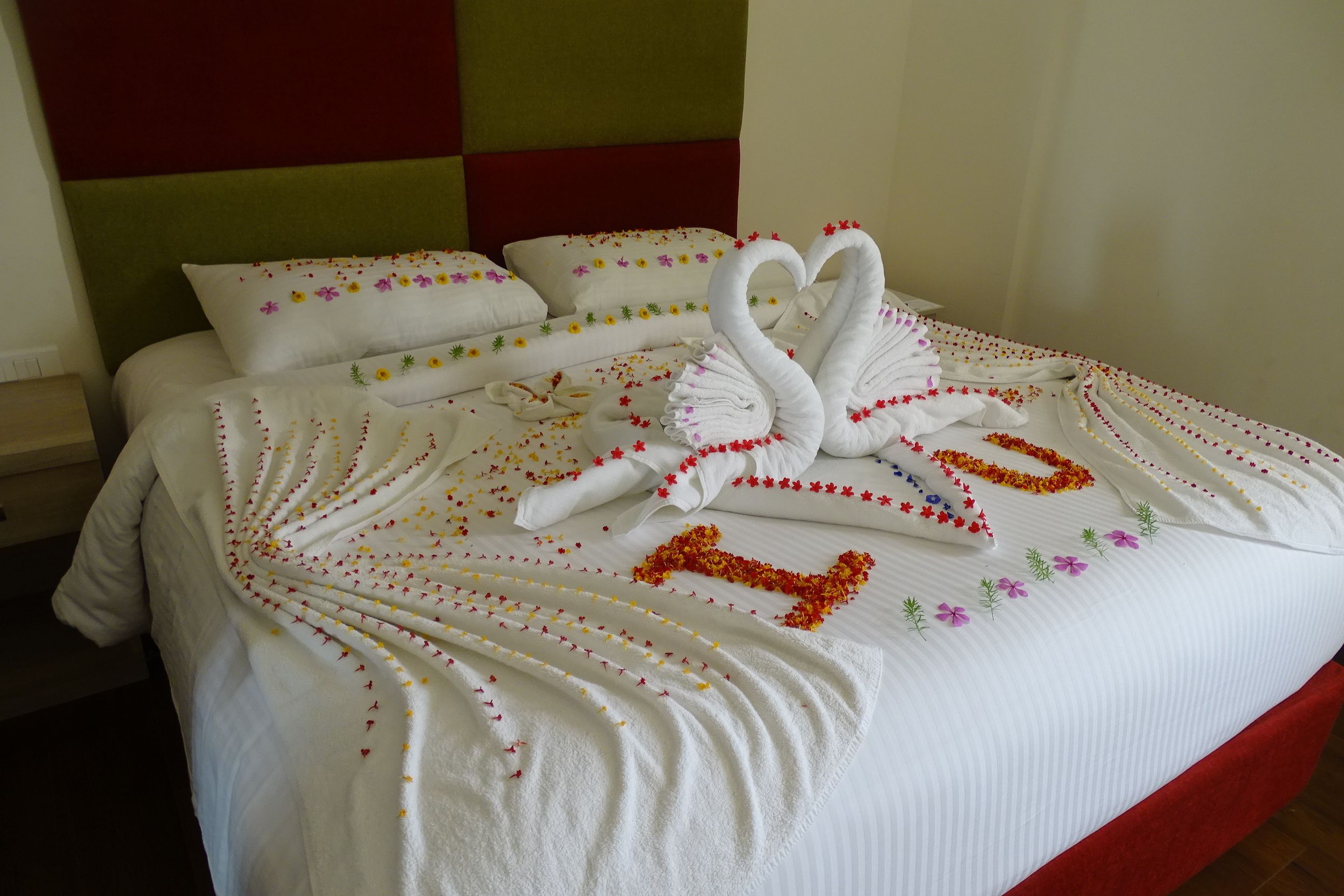 A neatly made bed with a swan-shaped towel arrangement and floral decorations.