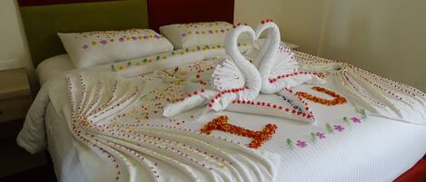 A neatly made bed with a swan-shaped towel arrangement and floral decorations.