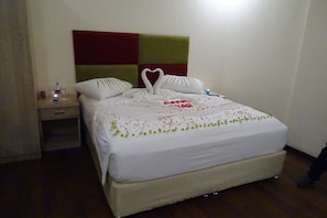 A neatly made bed with a heart-shaped decoration, a bedside table with a bottle, and a nightstand with a lamp. - Kanva Star Resorts (Bengaluru)