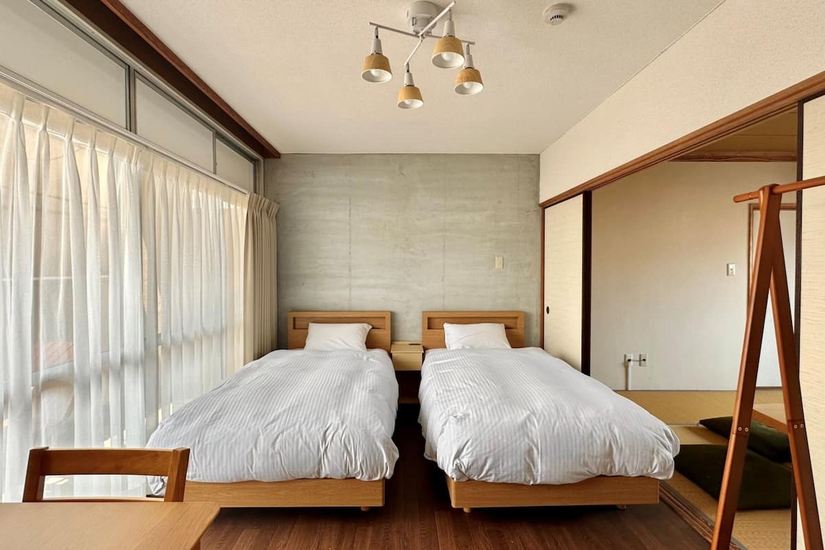 Ein modernes Hotelzimmer mit zwei Betten, einem Holztisch und einem großen Fenster mit durchsichtigen Vorhängen.