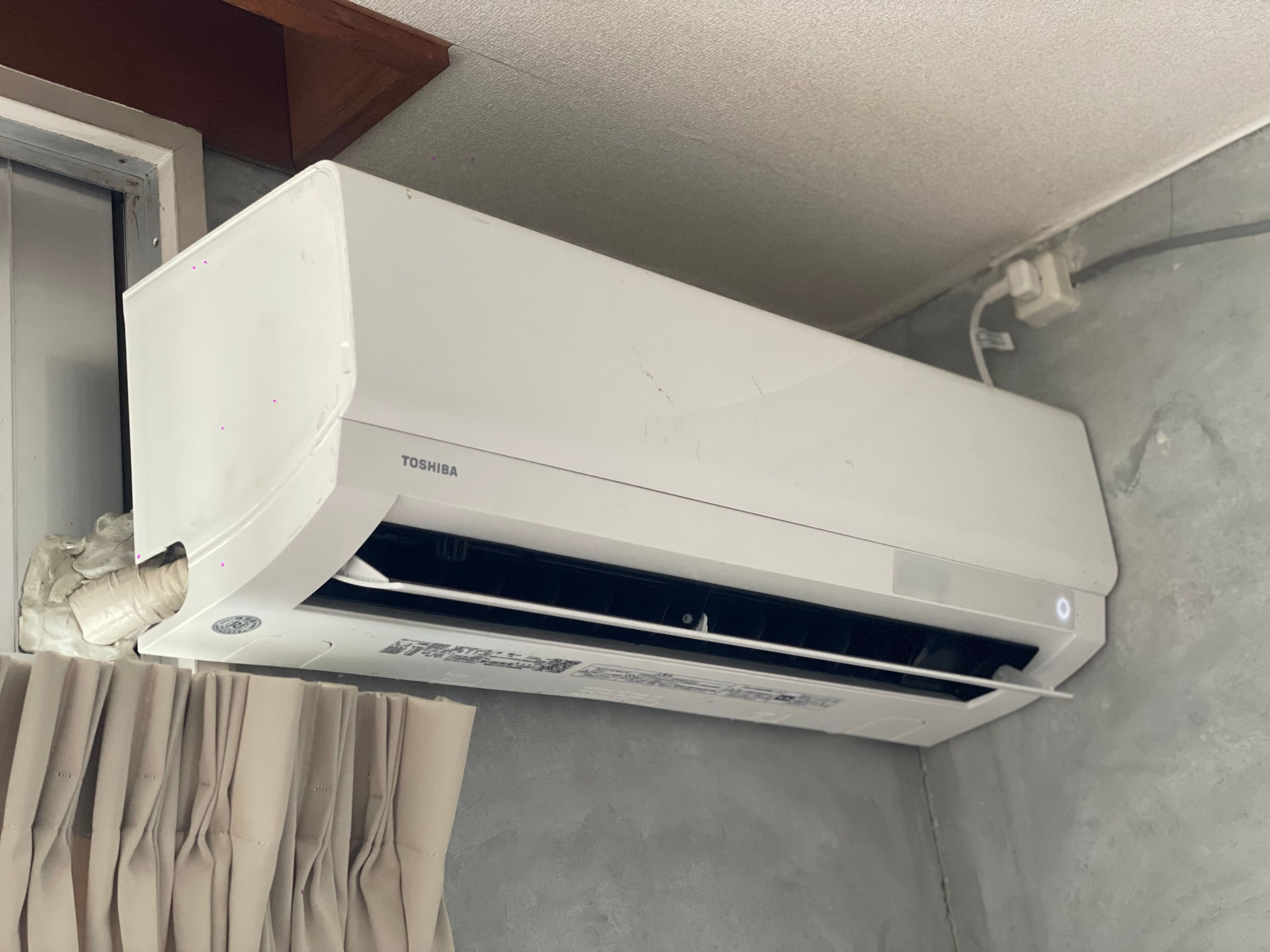 A white air conditioning unit mounted on a wall with a window above it.