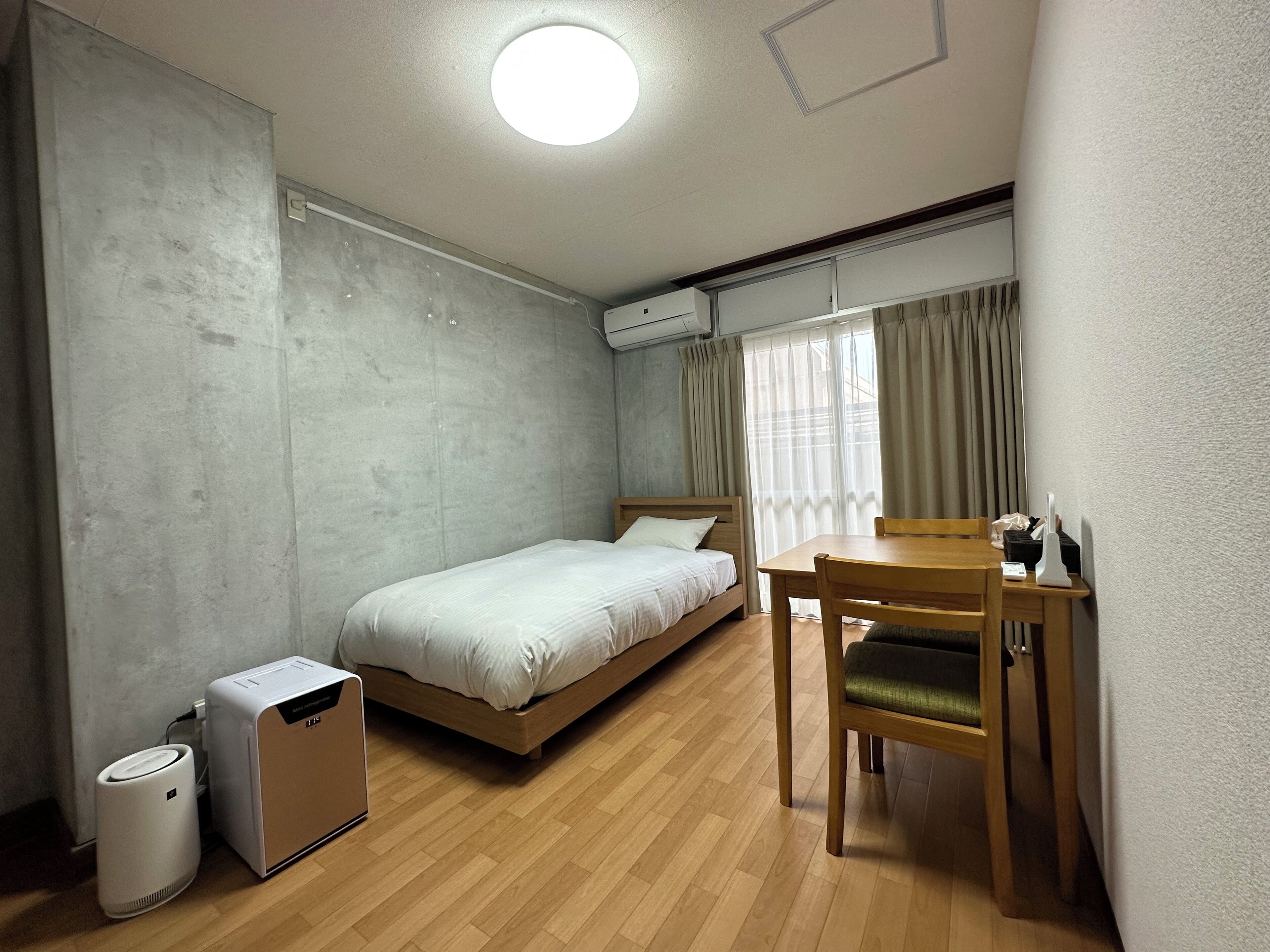 A compact room with a bed, a wooden desk, a chair, and an air purifier.