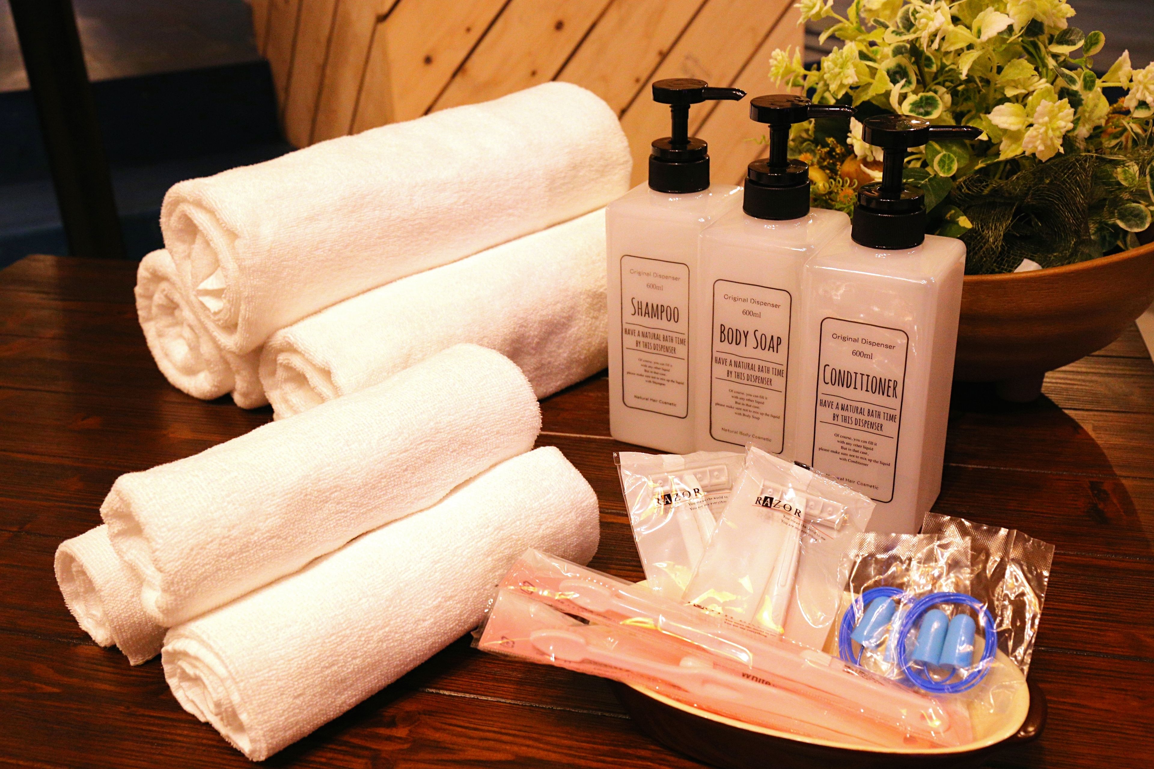 Neatly folded white towels, bottles of shampoo, body soap, and conditioner, along with a bowl of flowers and some toiletries on a wooden table.