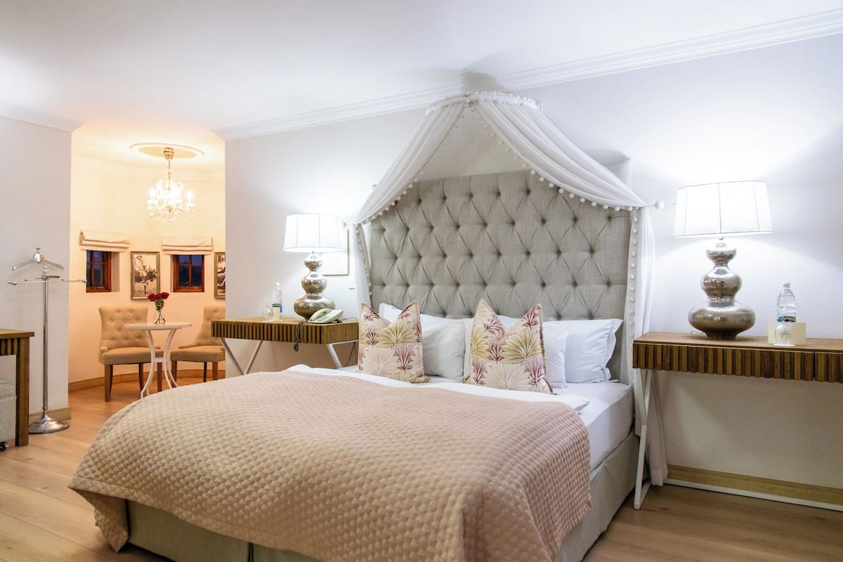 A bedroom with a tufted headboard, a canopy bed, bedside tables with lamps, a chair, and a desk.