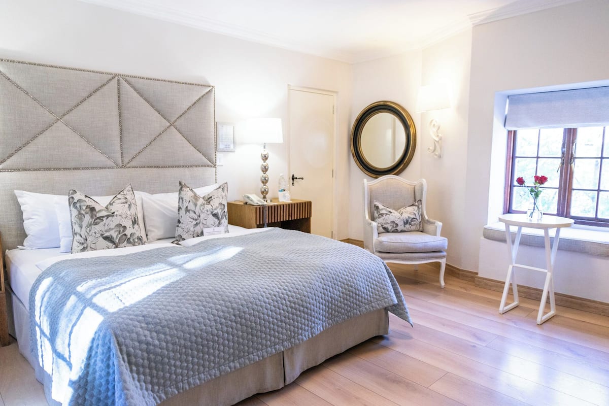 A bedroom with a large bed, a chair, a small table, and a window with a view.