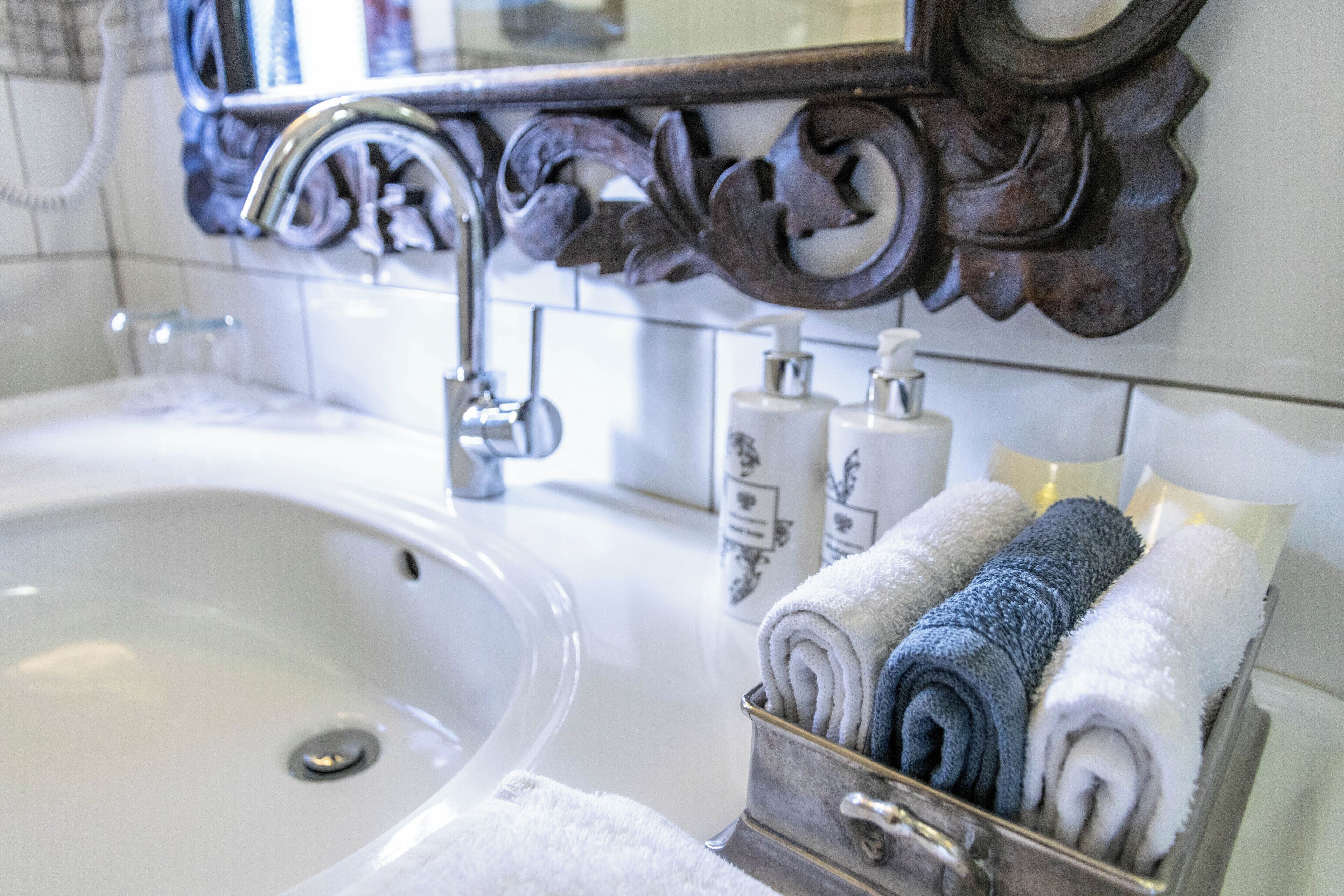 A bathroom with a white sink, a mirror with ornate woodwork, and a towel rack with neatly folded towels.