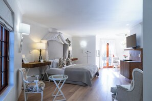 A hotel room with a bed, two chairs, a small table, a TV, and a window with curtains.
