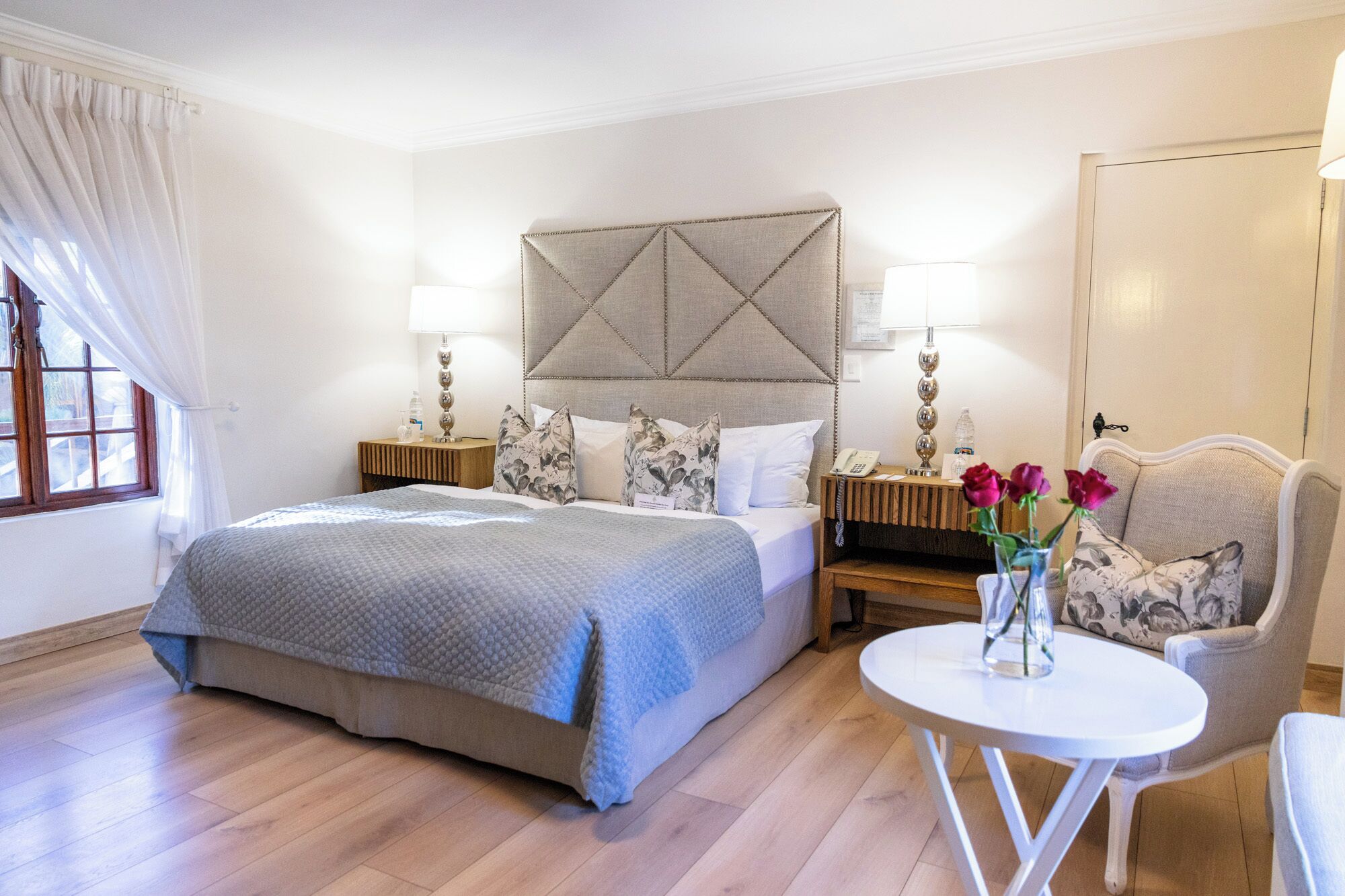 Habitación de hotel con una cama grande, dos mesitas de noche con lámparas, una mesita redonda y una silla.