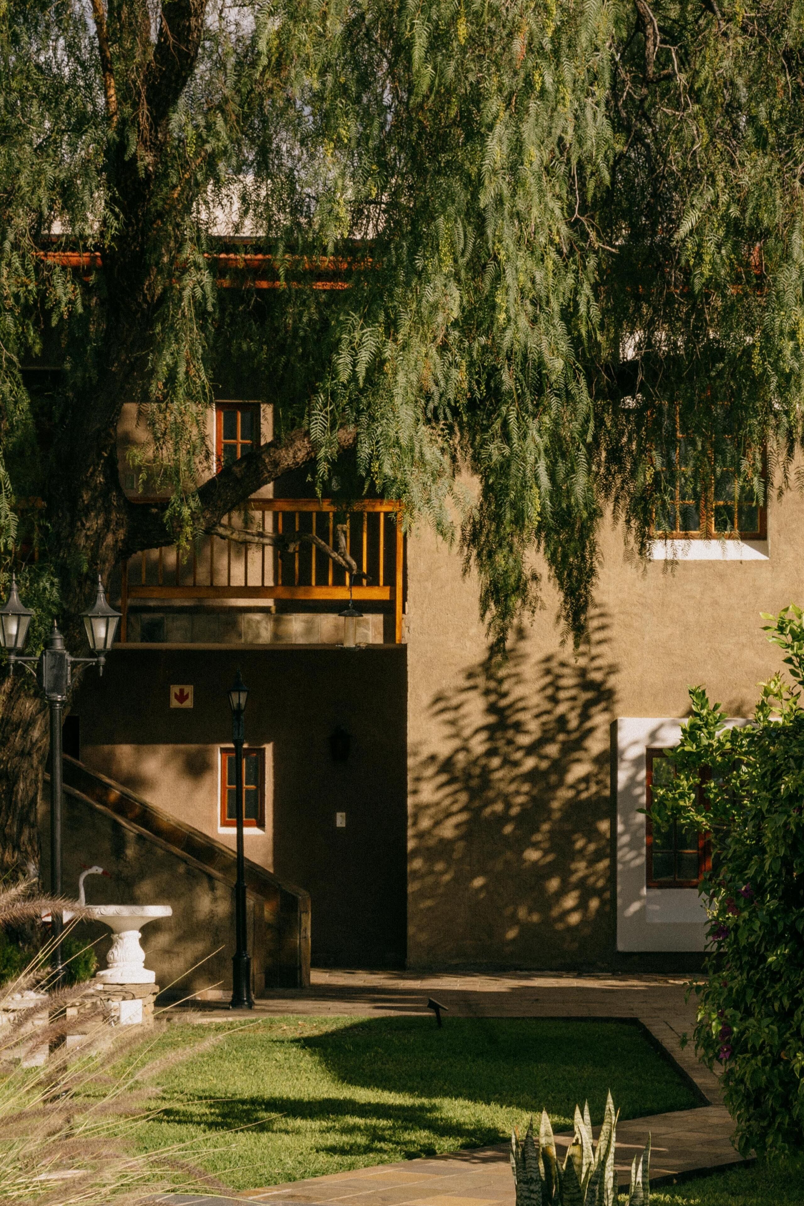 A building with a stone staircase leading to a balcony, surrounded by greenery.