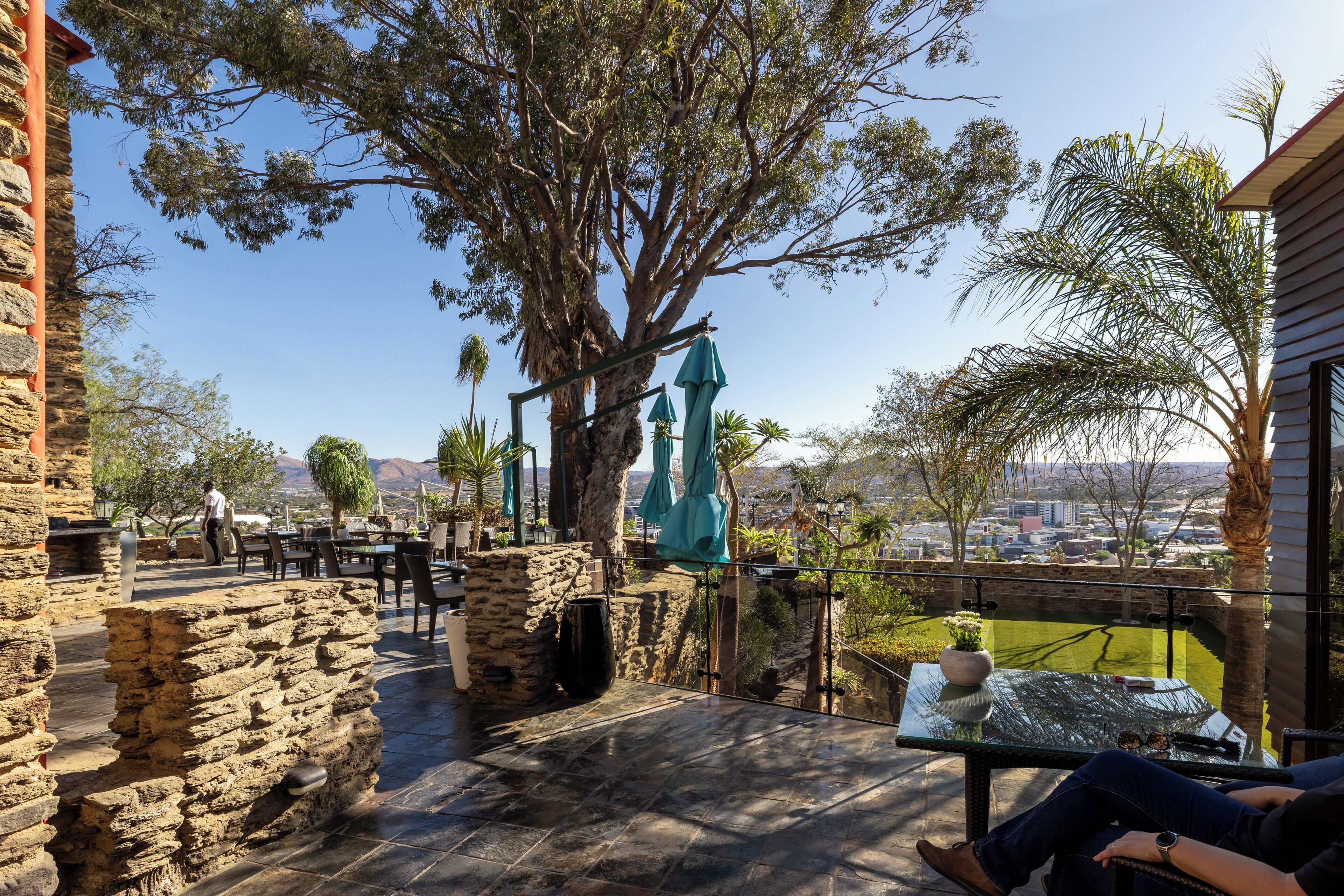 A patio area with stone walls, a table with a glass top, and a view of the cityscape.
