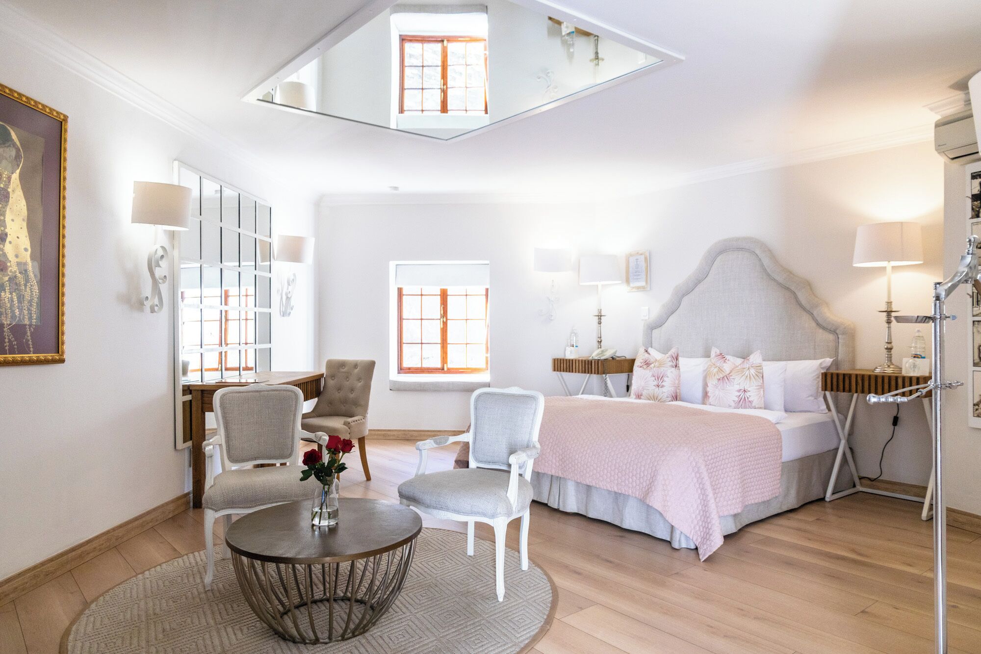 Quarto de hotel moderno com uma cama grande, dois poltronas, uma mesa de centro redonda e uma pequena mesinha de cabeceira.
