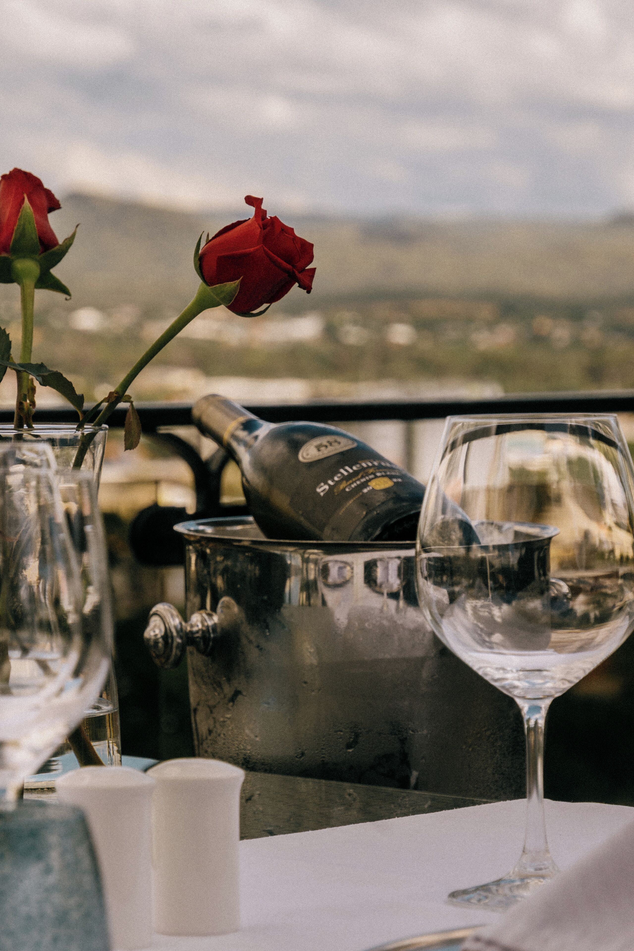 A table with a wine bottle, a wine glass, and a vase with a rose.