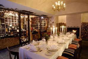 A long dining table set for a meal in a warmly lit room with a fireplace, wine racks, and a chandelier.
