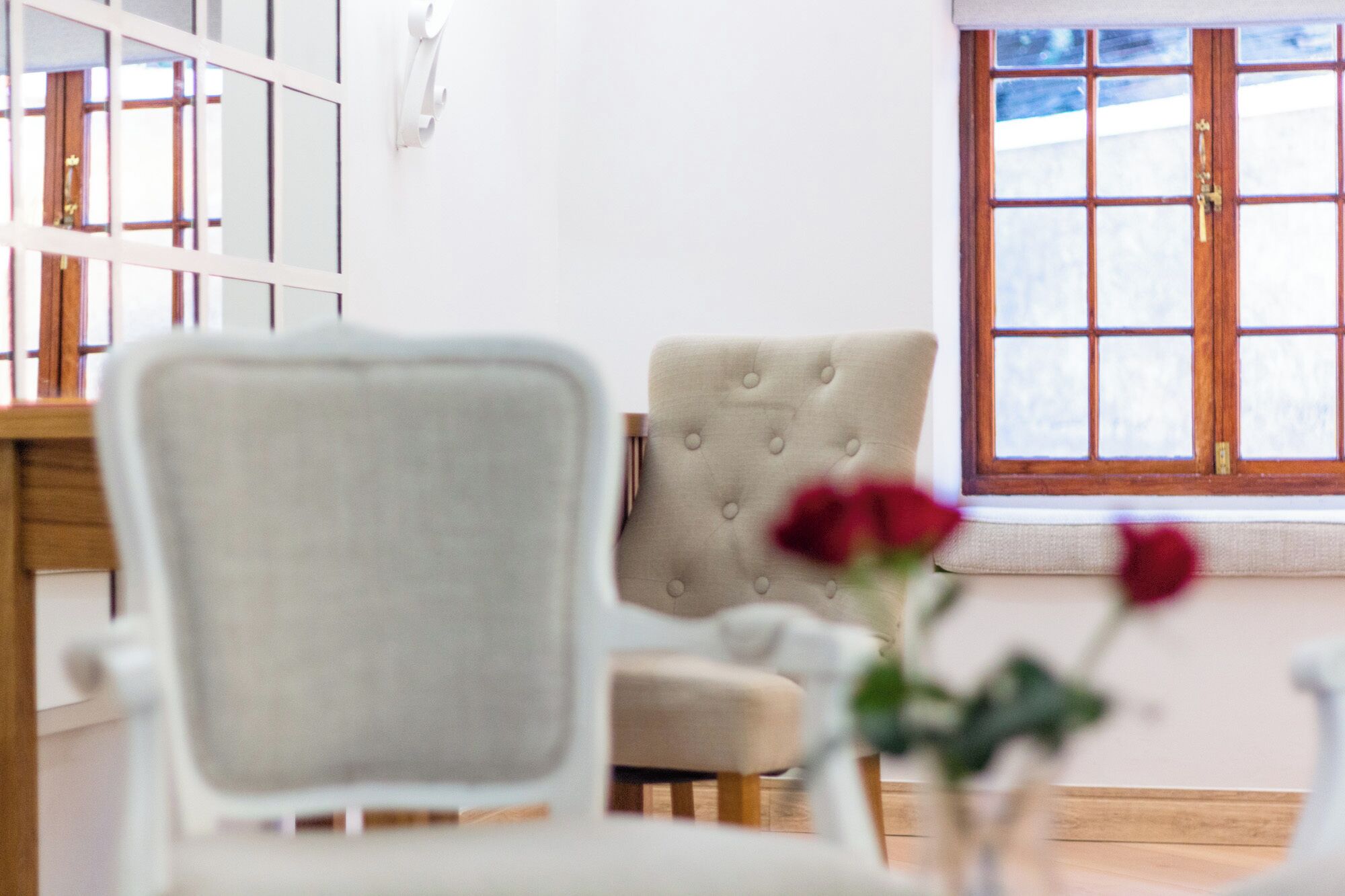 A room with a white chair, a tufted armchair, and a window with a view.