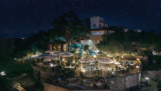 Une vue nocturne d’un hôtel avec des espaces de restauration en plein air, une tour et un ciel étoilé.