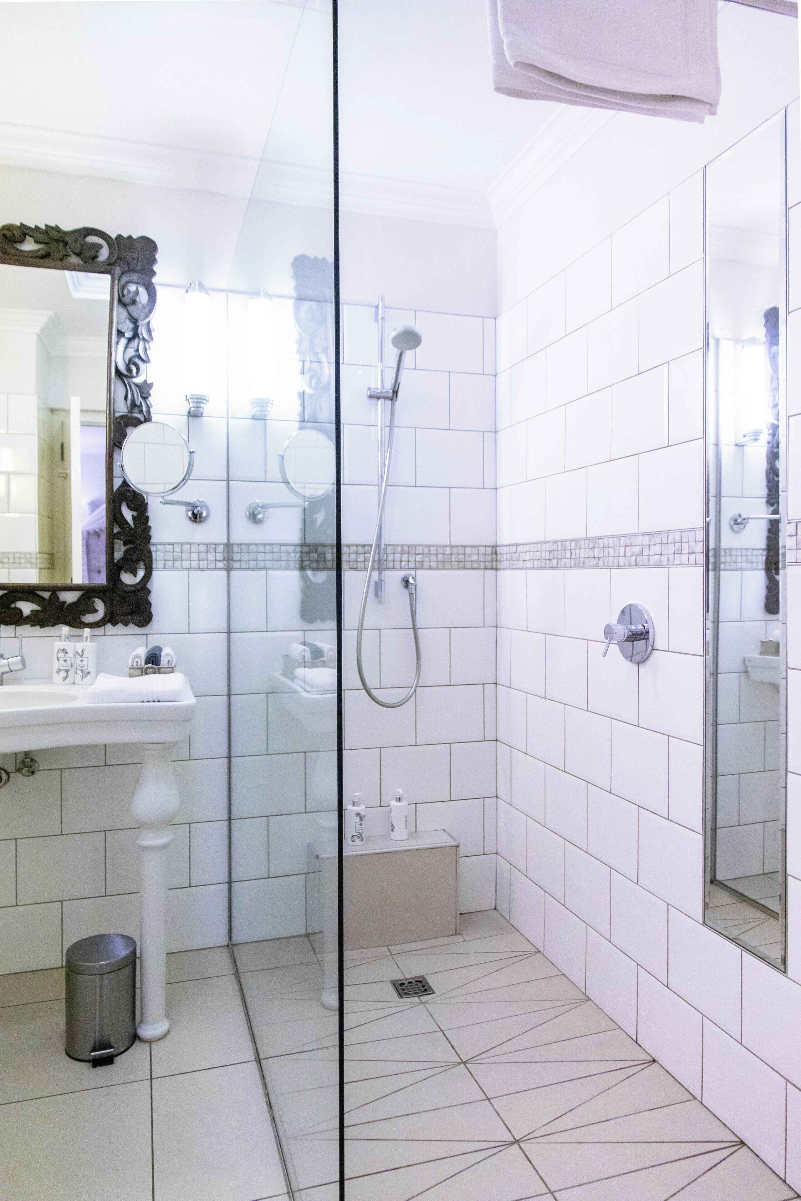Un baño con piso de baldosas blancas, un lavamanos con espejo y zona de ducha.