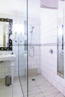 Un baño con piso de baldosas blancas, un lavamanos con espejo y zona de ducha.