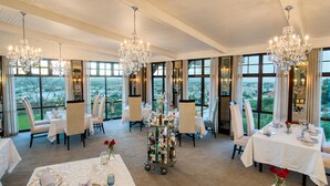 A dining area with tables set for four, large windows offering a city view, and ornate chandeliers. - Heinitzburg Boutique Hotel (Windhoek)