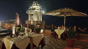 An outdoor dining area with tables, chairs, potted plants, and a pagoda-style building in the background.