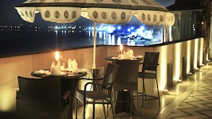 A terrace with tables and chairs, a decorative umbrella, and a view of a cityscape at night.