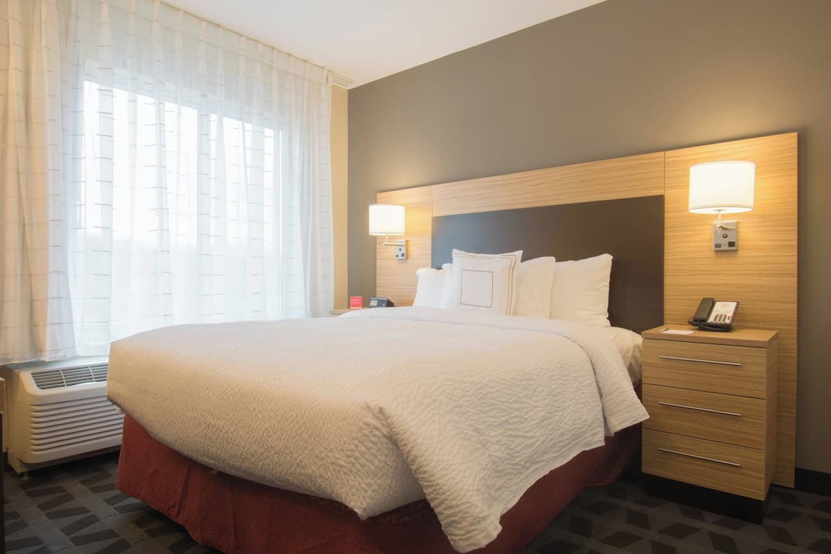 A hotel room with a large bed, two bedside lamps, a nightstand with a phone, and a window with curtains.